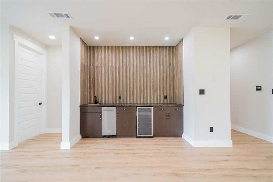 Built-in wet bar featuring a dark cabinetry base, stone-finish countertop, and wood-panel accent wall