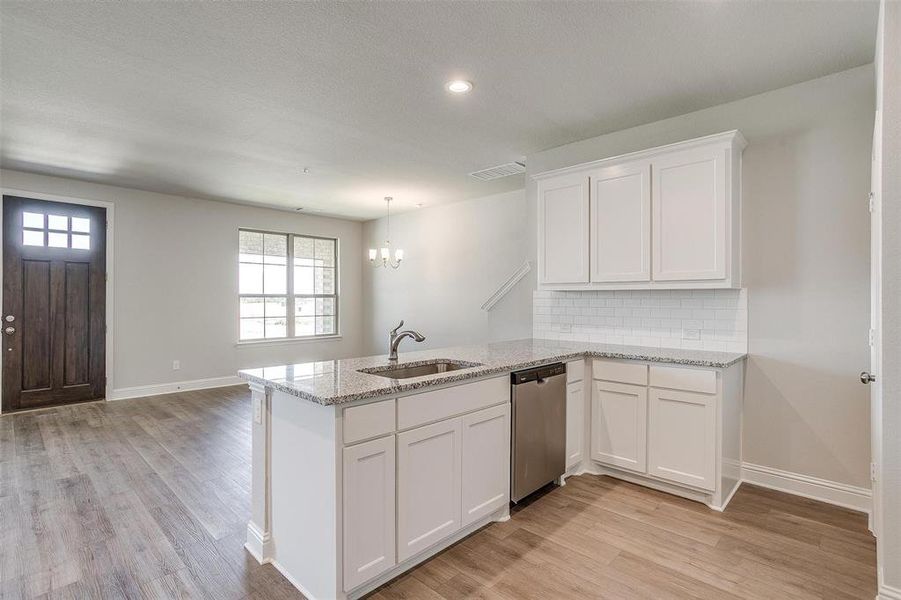 Kitchen featuring a peninsula, tasteful backsplash, white cabinets, hanging lights, and dishwasher