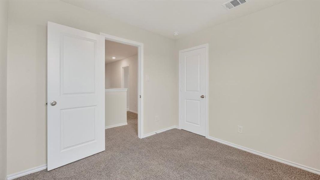 Carpeted room featuring light neutral wall paint, white baseboards, and white two-panel interior doors with brushed nickel hardware