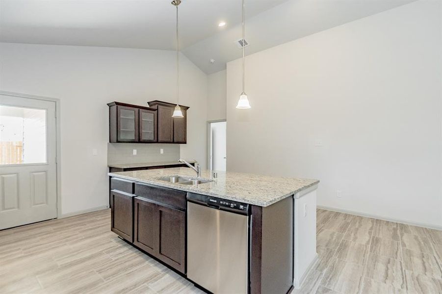 Sleek, modern, and functional, this view highlights the spacious kitchen, featuring an oversized island with stunning quartz countertops and a built-in stainless-steel dishwasher. Elegant pendant lighting enhances the contemporary vibe, while ample cabinet space ensures optimal storage. With easy access to the backyard and an open floor plan, this kitchen is designed for effortless entertaining and everyday living.