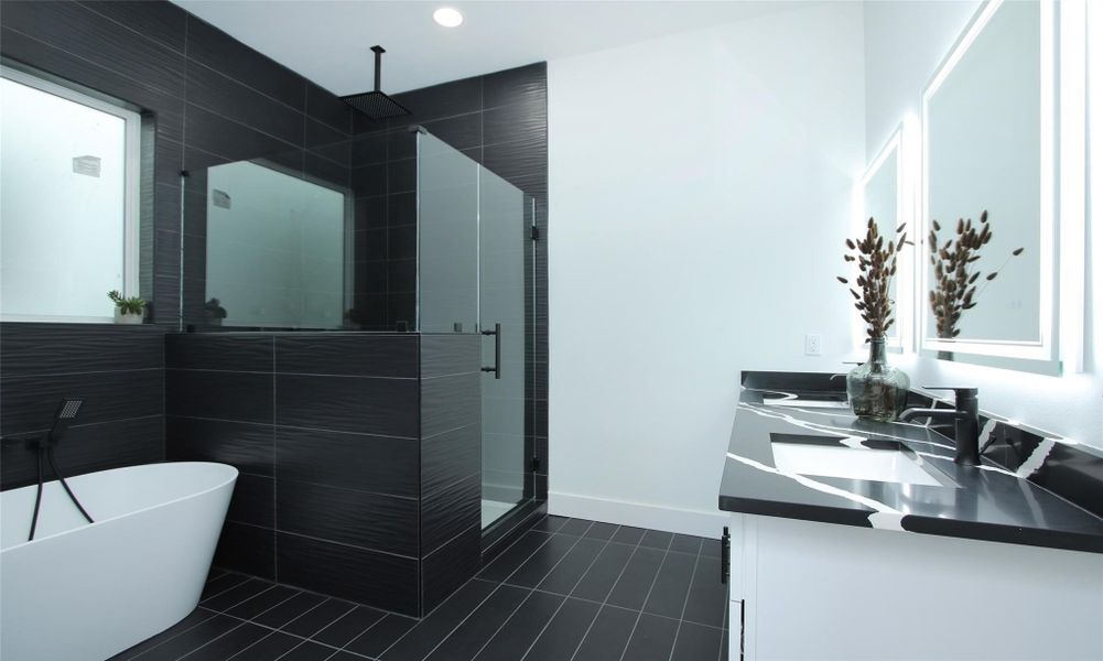 This primary bathroom features oversized black tiles, a spacious glass enclosed custom shower, a freestanding white tub, and a stylish dual-sink vanity with illuminated mirrors. This primary bathroom features oversized black tiles, a spacious glass enclosed custom shower, a freestanding white tub, and a stylish dual-sink vanity with illuminated mirrors.