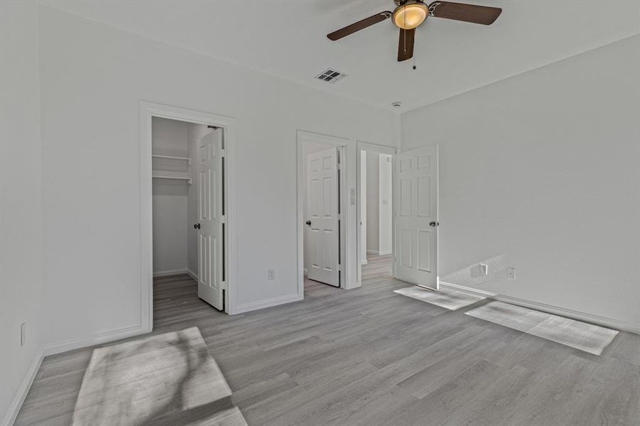 Unfurnished bedroom featuring light wood-type flooring, ceiling fan, and a walk in closet