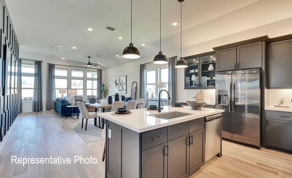 Open-concept kitchen and living area featuring wood-finish flooring, a kitchen island with integrated sink, stainless steel appliances, and ample natural light