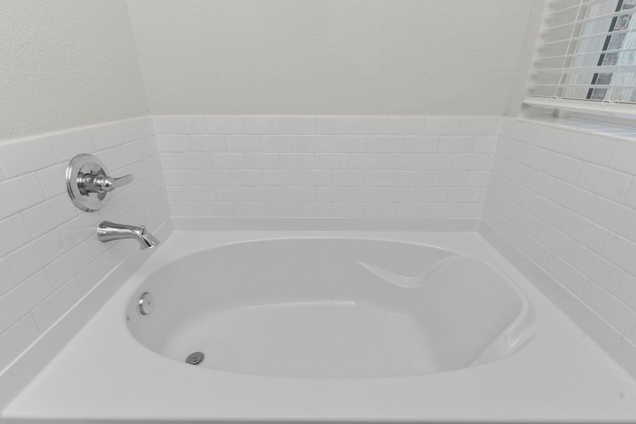 The primary bath offers a spa-like retreat featuring a deep soaking tub surrounded by crisp white tile—perfect for relaxing after a long day. Natural light fills the room, enhancing its fresh and calming atmosphere.