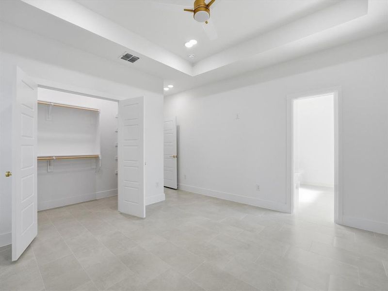 Unfurnished bedroom with a walk in closet, a raised ceiling, a ceiling fan, and recessed lighting