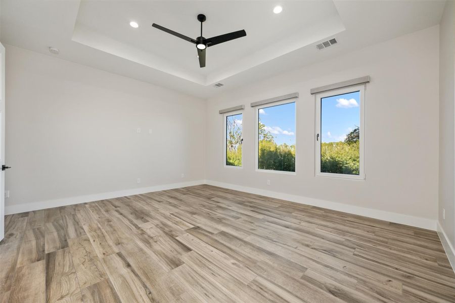 Spare room with ceiling fan, light hardwood / wood-style flooring, and a tray ceiling