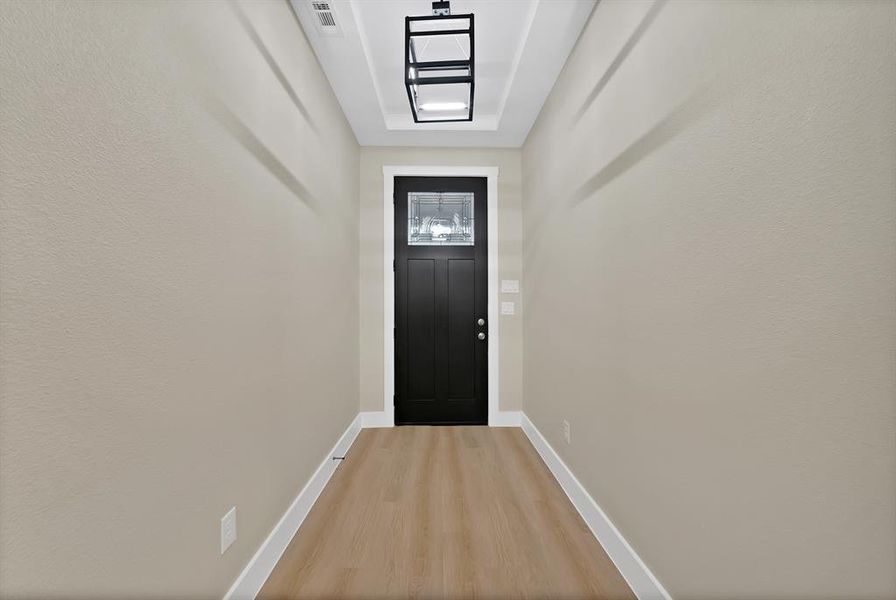 Entryway featuring a black paneled door with frosted glass inserts, wood-finish flooring, and light neutral walls Entryway featuring a black paneled door with frosted glass inserts, wood-finish flooring, and light neutral walls