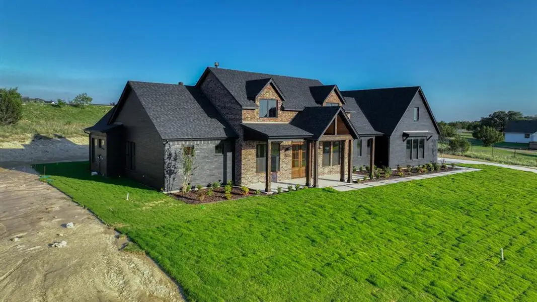 Modern farmhouse exterior featuring black siding, stone accents, a dark shingle roof, a covered entry with wood columns, and a landscaped front yard with new sod Modern farmhouse exterior featuring black siding, stone accents, a dark shingle roof, a covered entry with wood columns, and a landscaped front yard with new sod