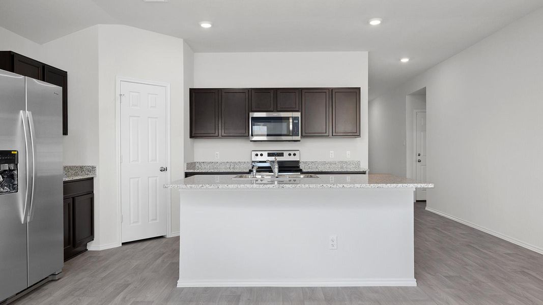Kitchen with stainless steel appliances, light stone countertops, a center island with sink, light wood finished floors, and recessed lighting