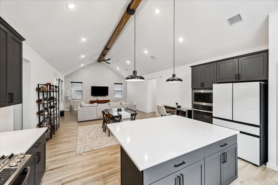Striking open-concept design anchored by soaring vaulted ceilings, an exposed wood beam, and expansive sightlines that seamlessly connect the kitchen, dining, and living spaces.