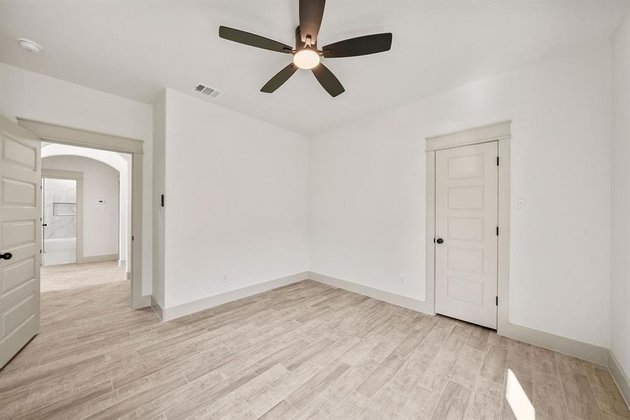Empty room with light wood-style floors, arched walkways, and ceiling fan
