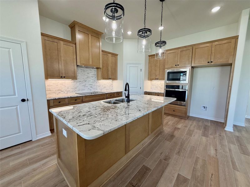 Kitchen featuring tasteful backsplash, light stone countertops, hanging light fixtures, wood finish floors, and stainless steel appliances