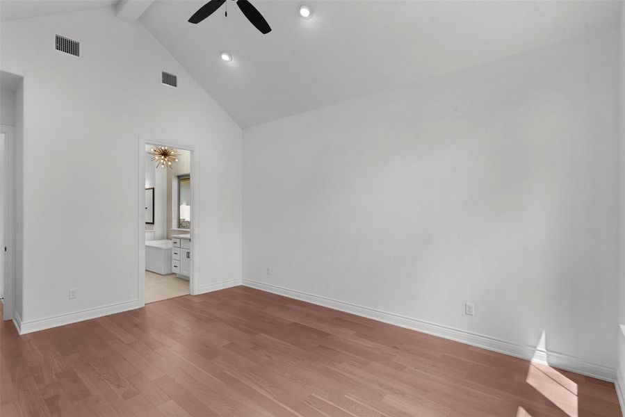 Hardwood floors and a vaulted ceiling elevate this primary bedroom, leading to a well-appointed primary bath.