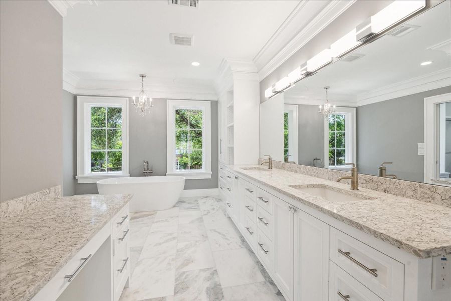 The luxurious primary bathroom features a double vanity with marble countertops, elegant light fixtures, a freestanding bathtub, and large windows providing ample natural light.