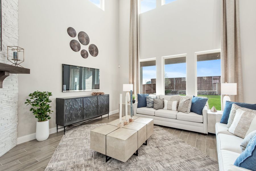 Living room with two-story ceiling, white sofas, stone fireplace, and large windows with backyard view Living room with two-story ceiling, white sofas, stone fireplace, and large windows with backyard view