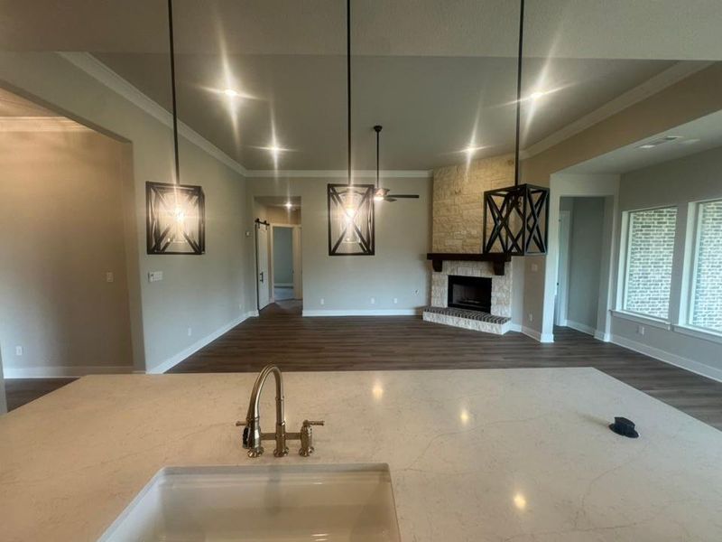 Spacious living area featuring wood-finish flooring, a stone fireplace with a wood mantle, and three large windows