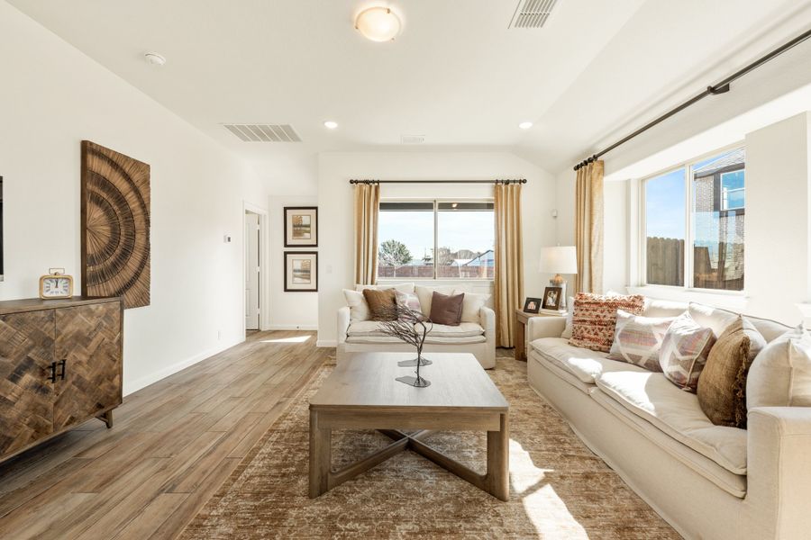 Living room with hardwood floors, white sofas, wood coffee table, and large windows with gold curtains