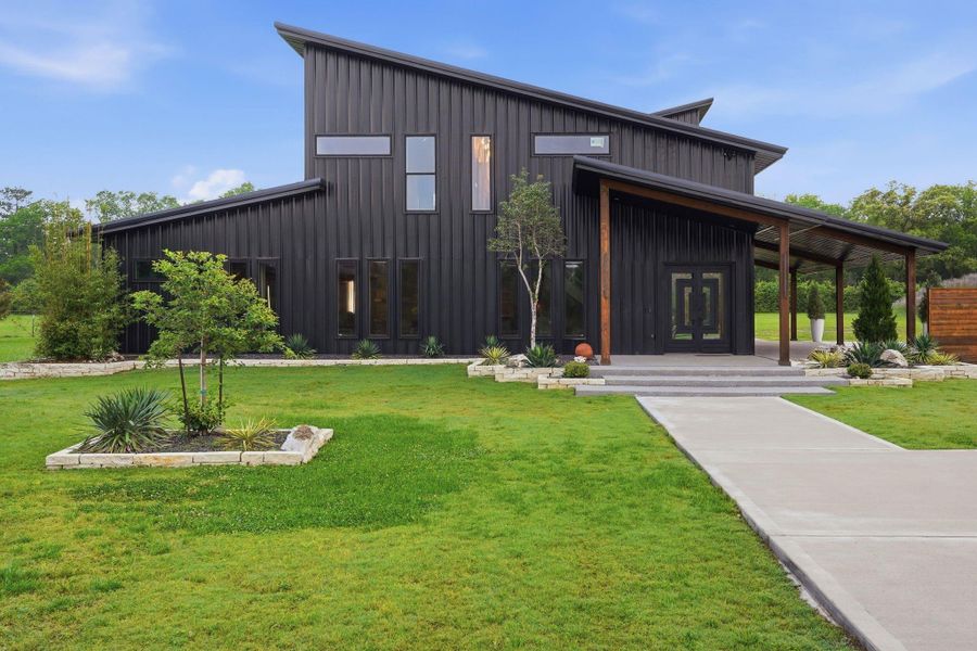 This modern home features a sleek, angular design with a dark exterior. It has large windows for natural light and a spacious covered entryway. The well-maintained lawn and minimalist landscaping add to its contemporary appeal.