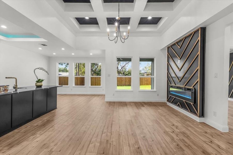 Unfurnished living room featuring a chandelier, light wood finished floors, coffered ceiling, beamed ceiling, and recessed lighting
