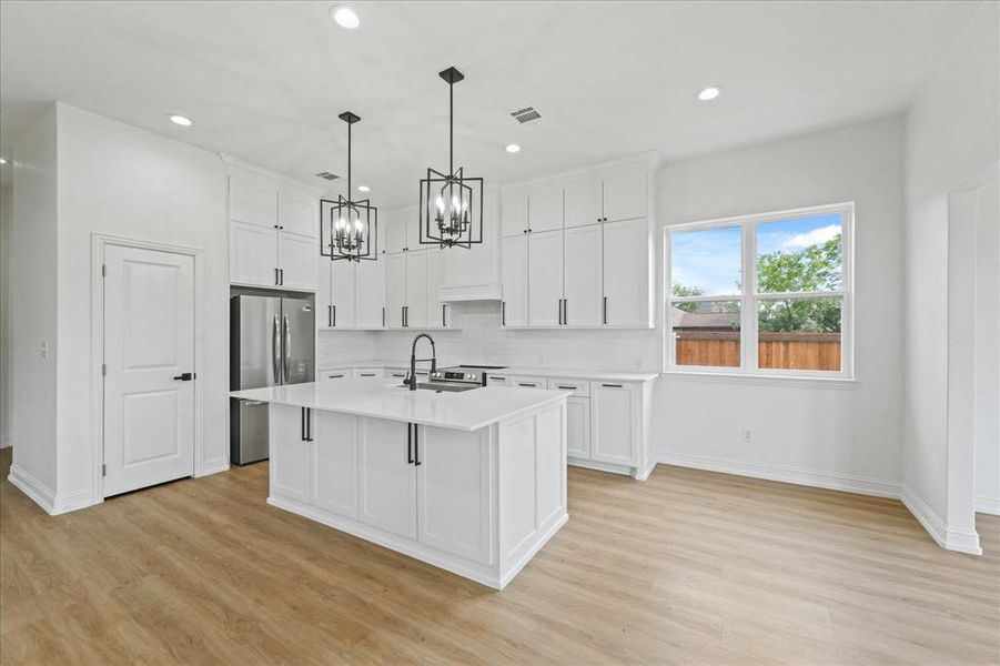 Modern kitchen featuring white shaker cabinetry, stainless steel appliances, a center island with a sink, and pendant lighting