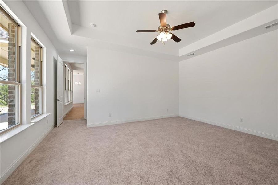 Empty room with ceiling fan, light carpet, and a raised ceiling