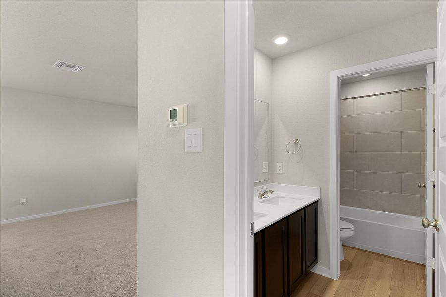 Bathroom with double vanity, bathing tub / shower combination, and light wood-style flooring