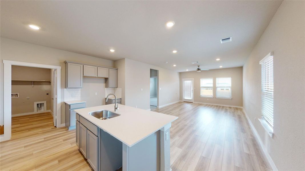 Kitchen with gray cabinetry, light wood finished floors, an island with sink, and recessed lighting