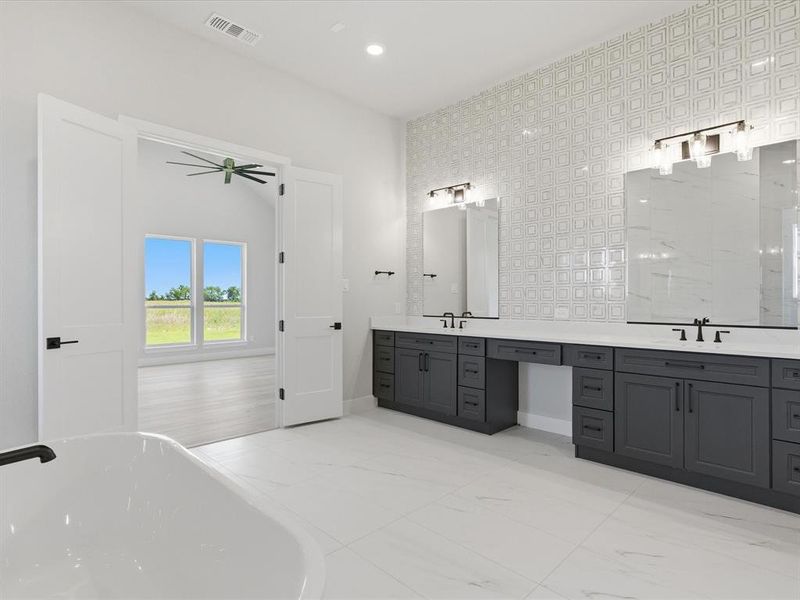 Spacious bathroom featuring a freestanding soaking tub, dual vanity with dark cabinetry, integrated makeup area, and white patterned wall tile