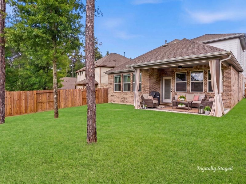 Expansive fenced backyard with a covered rear patio and mature shade trees. The wooded backdrop offers added privacy and a serene setting for outdoor living. This photo has been digitally staged to illustrate the possibilities of the home's aesthetic and potential design. Some furnishings and décor shown are for visual inspiration.