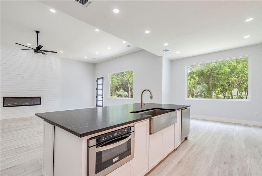 Kitchen with open floor plan, light wood-type flooring, dark countertops, white cabinetry, and a fireplace Kitchen with open floor plan, light wood-type flooring, dark countertops, white cabinetry, and a fireplace