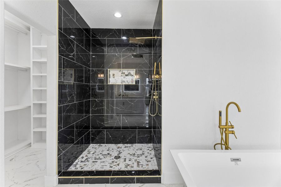 Elegant freestanding tub with a brass faucet complements the luxurious walk-in shower and nearby shelving.