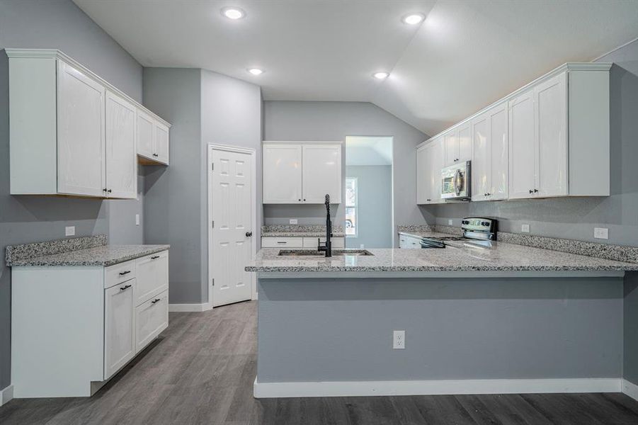 Kitchen with vaulted ceiling, light stone countertops, white cabinetry, dark wood-style flooring, and appliances with stainless steel finishes Kitchen with vaulted ceiling, light stone countertops, white cabinetry, dark wood-style flooring, and appliances with stainless steel finishes