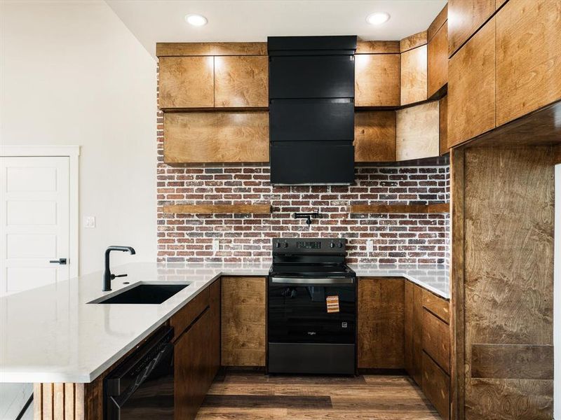 Kitchen featuring a peninsula, black appliances, dark wood finished floors, light stone counters, and backsplash Kitchen featuring a peninsula, black appliances, dark wood finished floors, light stone counters, and backsplash