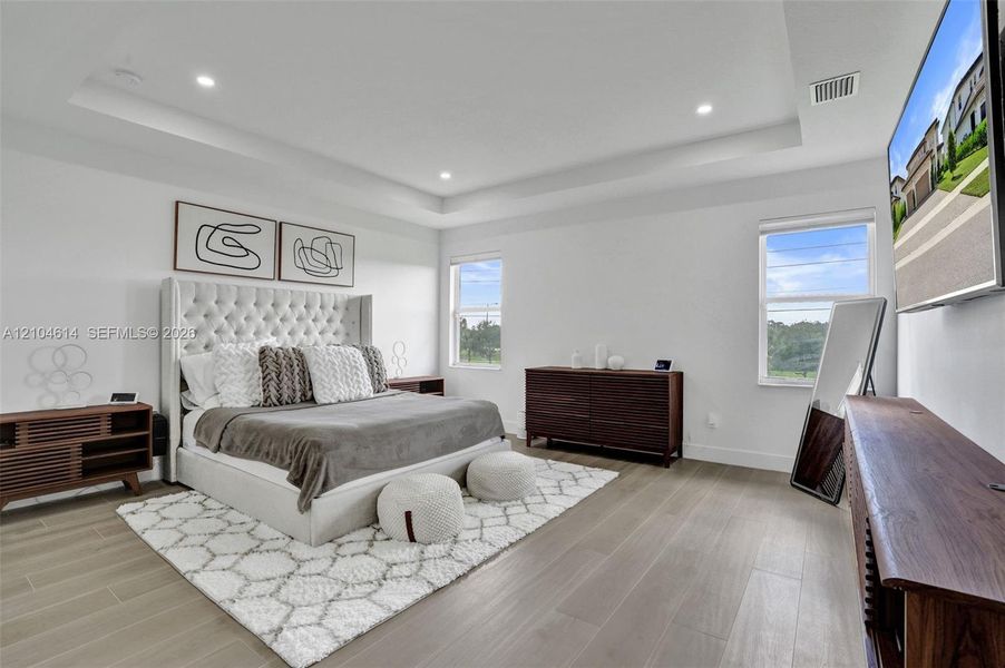 Tray ceiling with recessed lighting, wood look flooring, and multiple windows