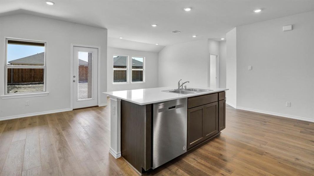 Kitchen with a kitchen island with sink, stainless steel dishwasher, dark wood finish cabinetry, lofted ceiling, and dark wood-style floors