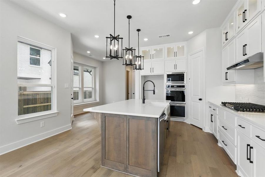 Kitchen featuring white cabinetry, glass insert cabinets, a center island with sink, recessed lighting, and dark wood-style floors
