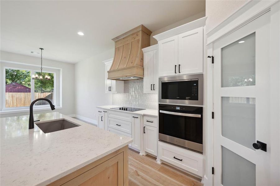 Kitchen featuring white cabinetry, oven, hanging light fixtures, and sink