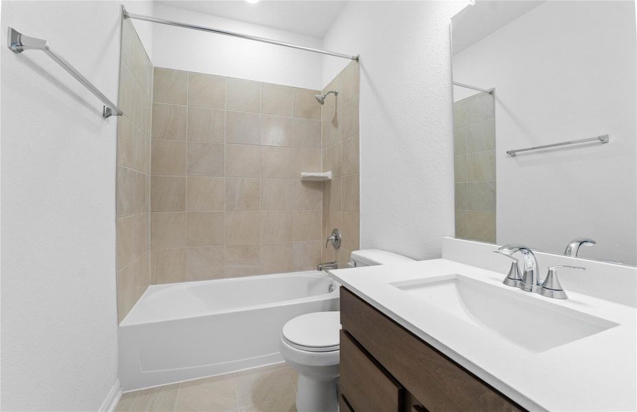 The secondary bathroom showcases tile flooring, a bath/shower combo with Daltile tile surround, a vanity with stunning light countertop, a mirror, sleek fixtures, and contemporary finishes throughout.
