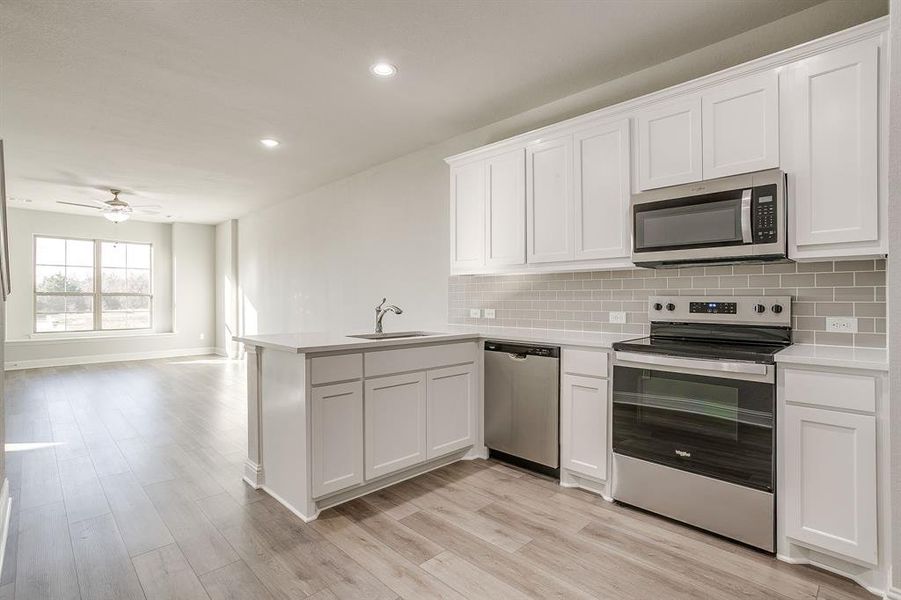 Kitchen featuring stainless steel appliances, white cabinets, a ceiling fan, a peninsula, and light wood finished floors Kitchen featuring stainless steel appliances, white cabinets, a ceiling fan, a peninsula, and light wood finished floors