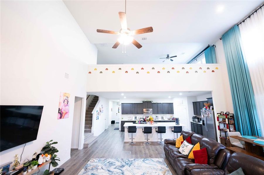 Open-concept living space featuring high ceilings, wood-finish flooring, and a modern kitchen with a large island and dark cabinetry Open-concept living space featuring high ceilings, wood-finish flooring, and a modern kitchen with a large island and dark cabinetry