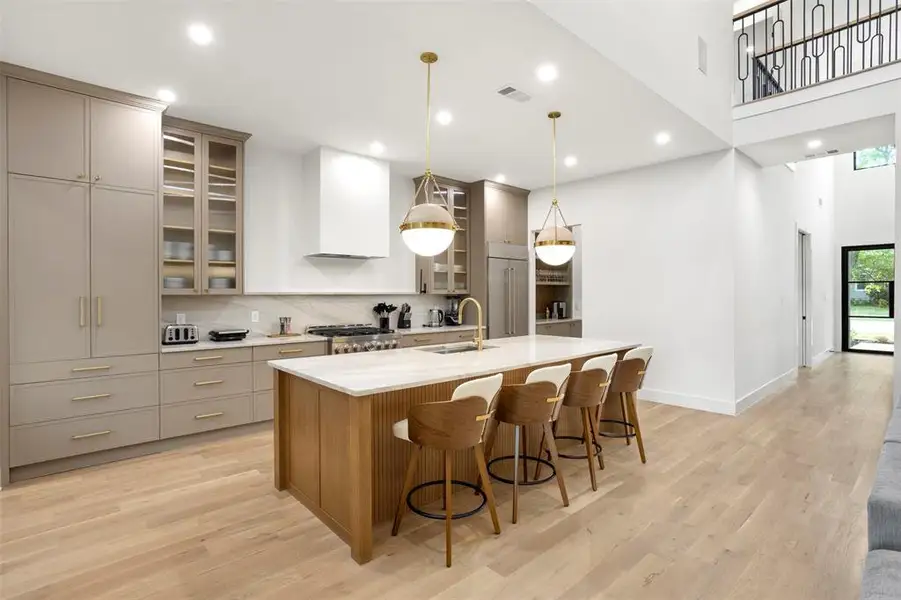Gourmet kitchen featuring a large central island with seating, a professional-grade range, custom cabinetry, a built-in refrigerator, and wood-finish flooring