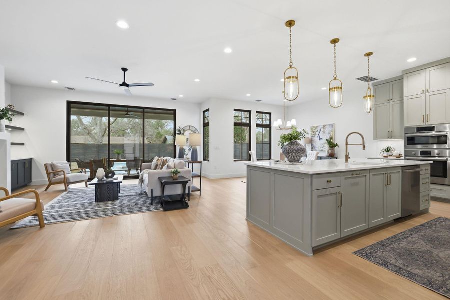 Kitchen featuring gray cabinetry, open floor plan, light wood-style floors, stainless steel appliances, and a center island with sink