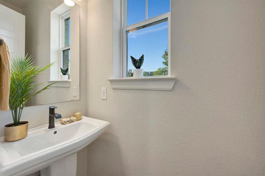 Pedestal sink with a matte black faucet, wall-mounted mirror, and a window with natural light