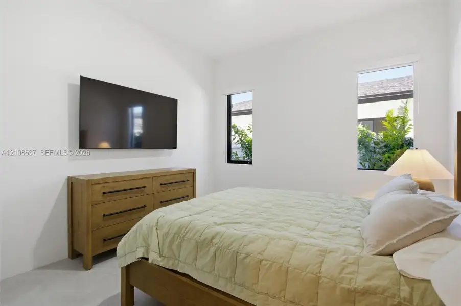 Neutral-toned bedroom featuring minimalist interior design, large rectangular windows with black frames, and recessed lighting