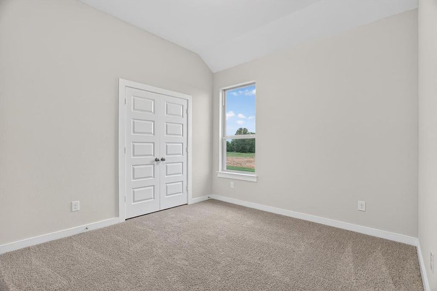 Vaulted ceiling room featuring light neutral wall tones, plush carpeting, white baseboards, and a large window with outdoor scenery