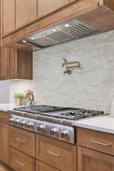 Kitchen with stainless steel gas cooktop, custom range hood, brown cabinets, and backsplash