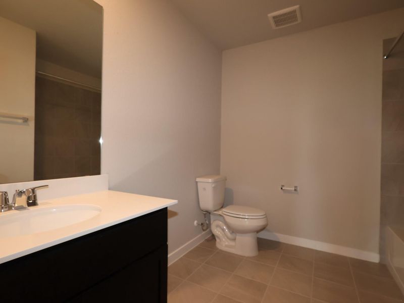 A well-appointed bathroom offers a sleek vanity and tiled flooring, reflecting simple elegance.