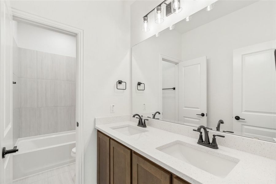 Bathroom with double sink vanity, dark wood cabinets, quartz countertop, and tiled shower-tub combo Bathroom with double sink vanity, dark wood cabinets, quartz countertop, and tiled shower-tub combo