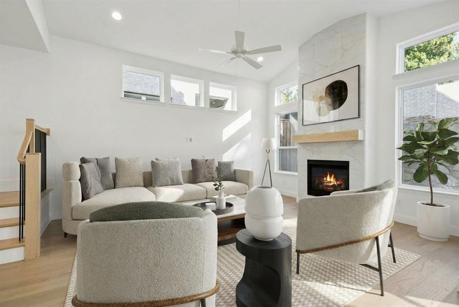 Living room featuring vaulted ceiling, plenty of natural light, a tiled fireplace, light wood-style floors, and a ceiling fan Living room featuring vaulted ceiling, plenty of natural light, a tiled fireplace, light wood-style floors, and a ceiling fan