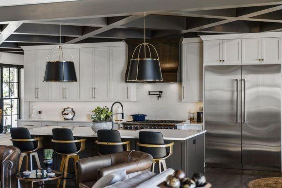 Kitchen with built in refrigerator, coffered ceiling, white cabinetry, a center island with sink, and wall chimney exhaust hood